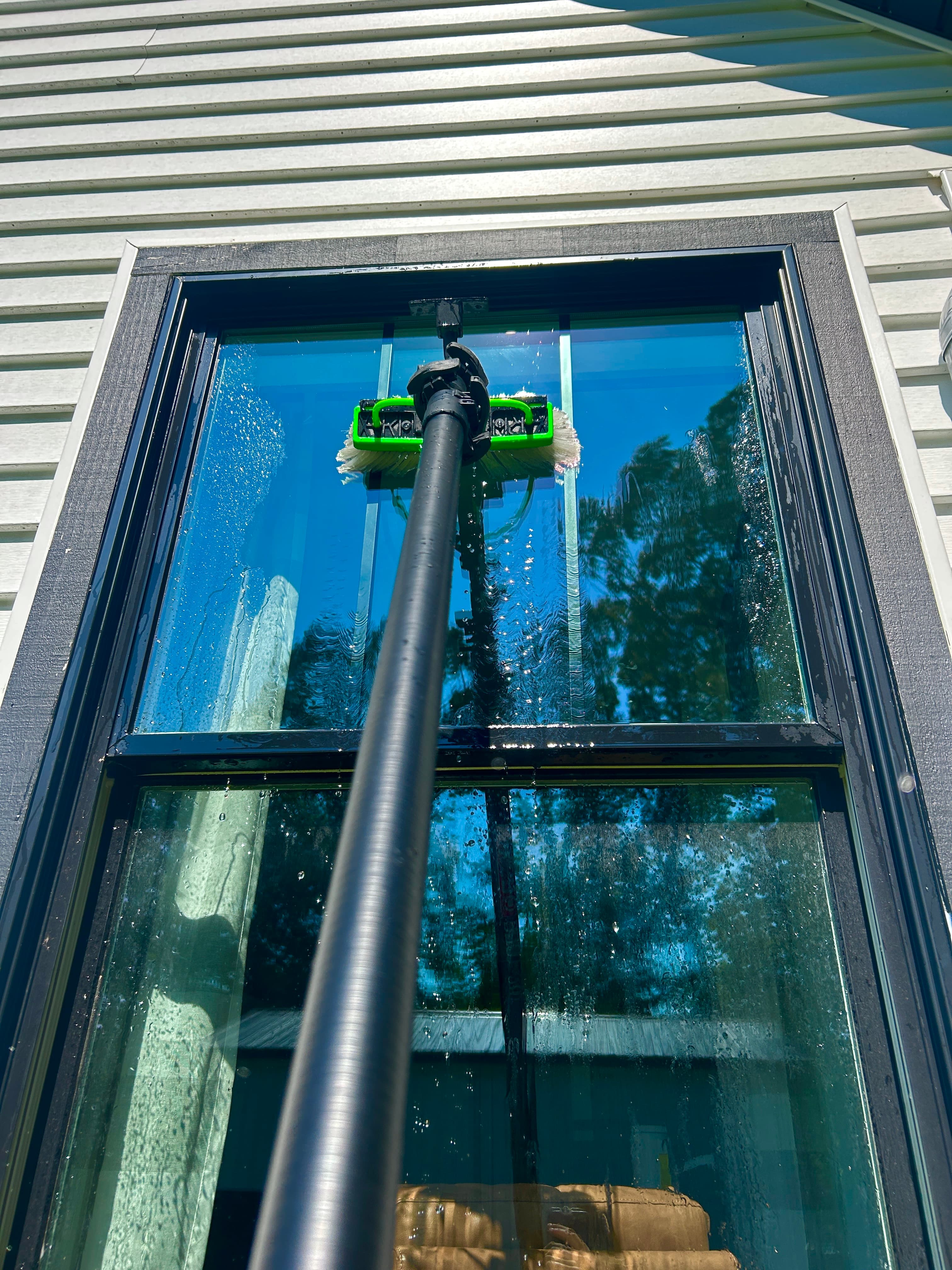 Water-fed pole brush cleaning a second-story window from the ground