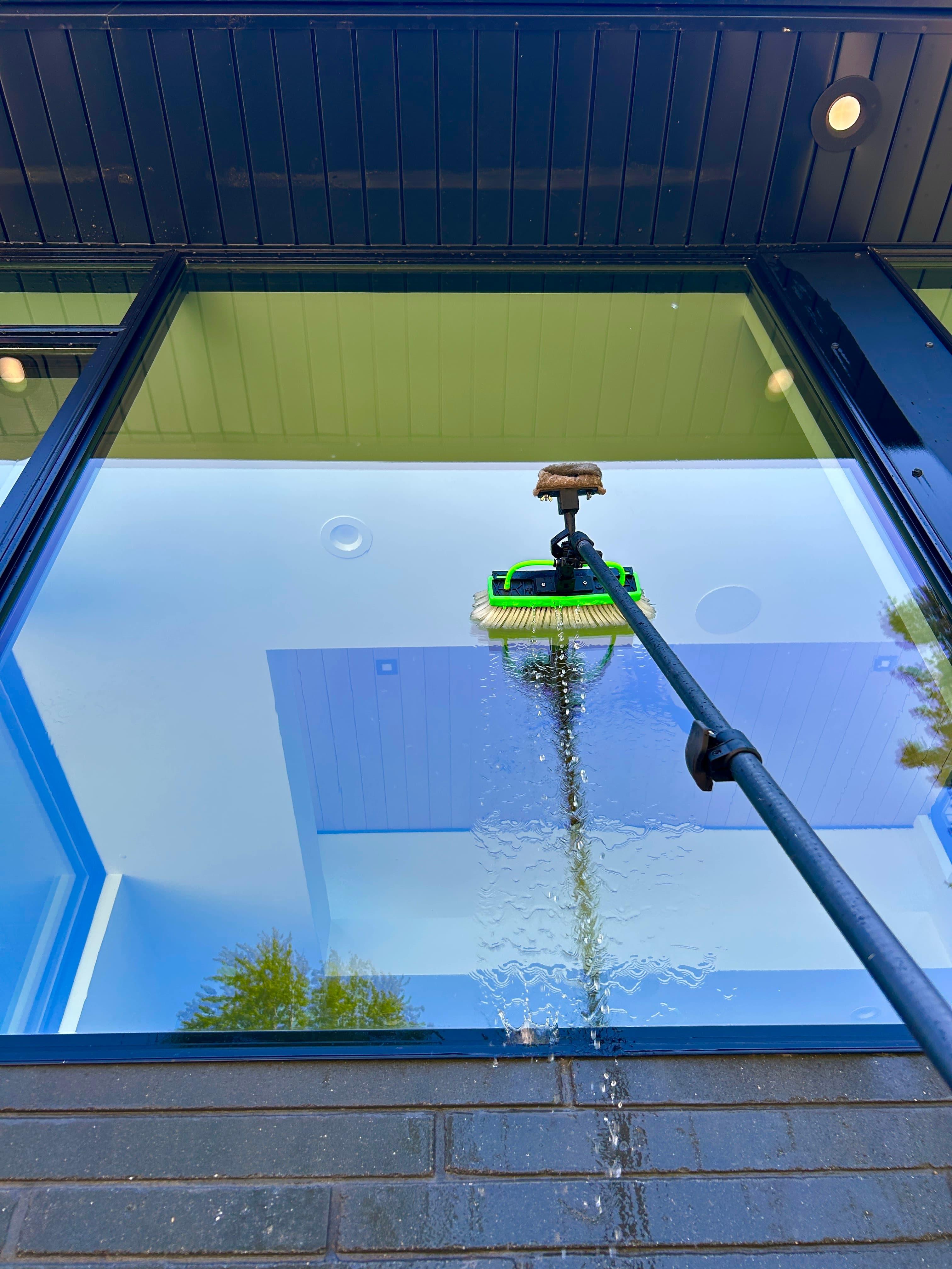Water-fed pole brush cleaning an overhead skylight