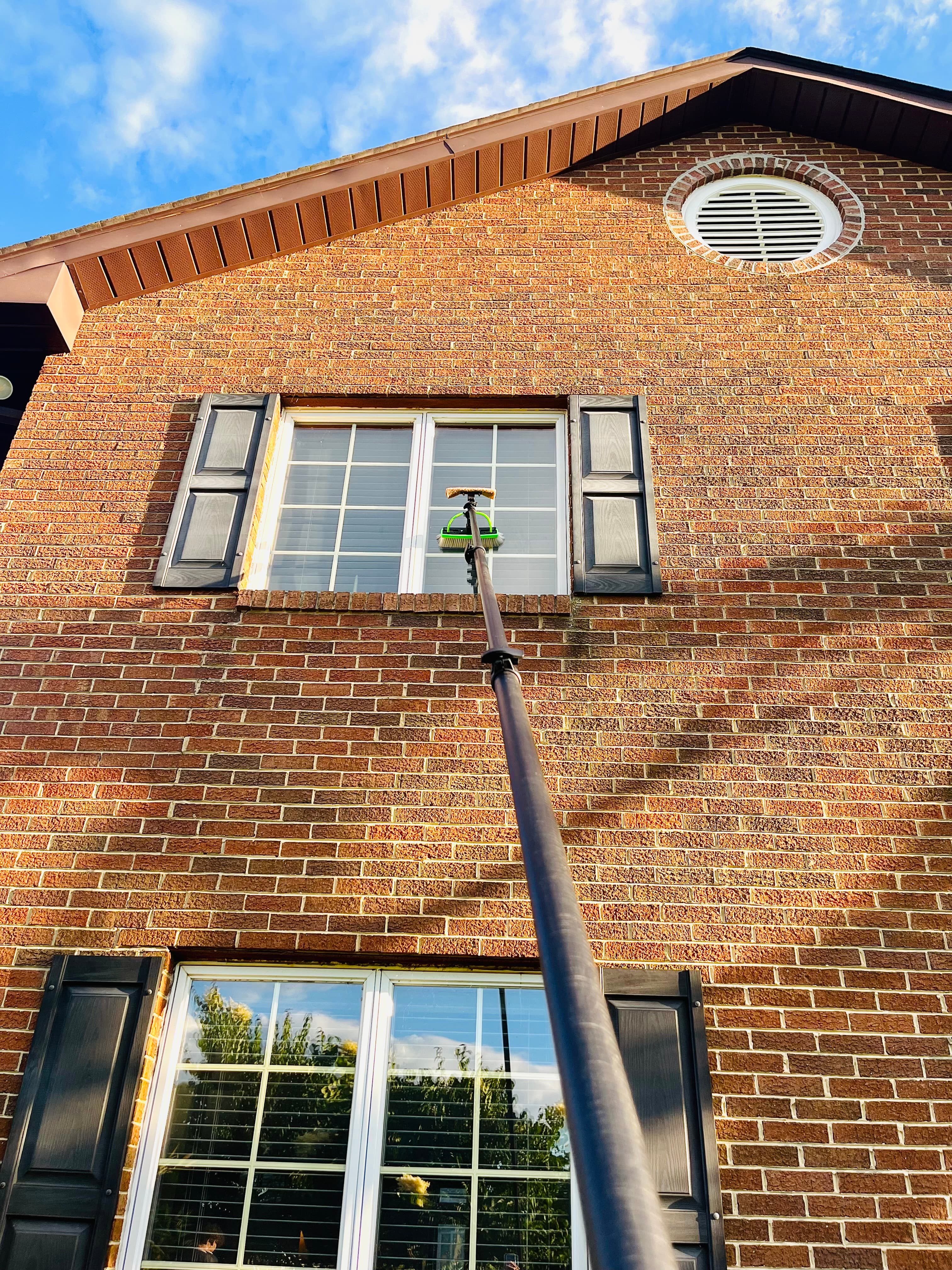Extension-pole window cleaning on a second-story brick home window